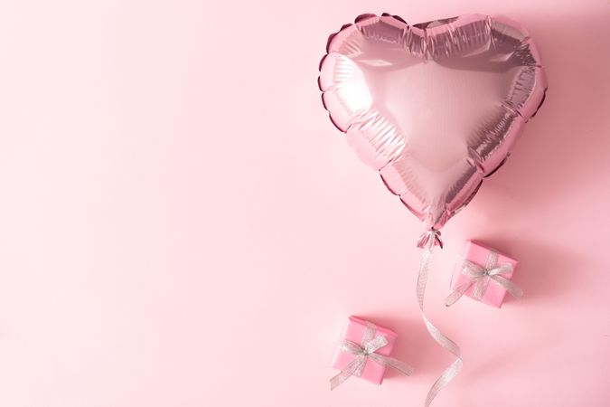 Pink foil balloon and wrapped presents against pink background