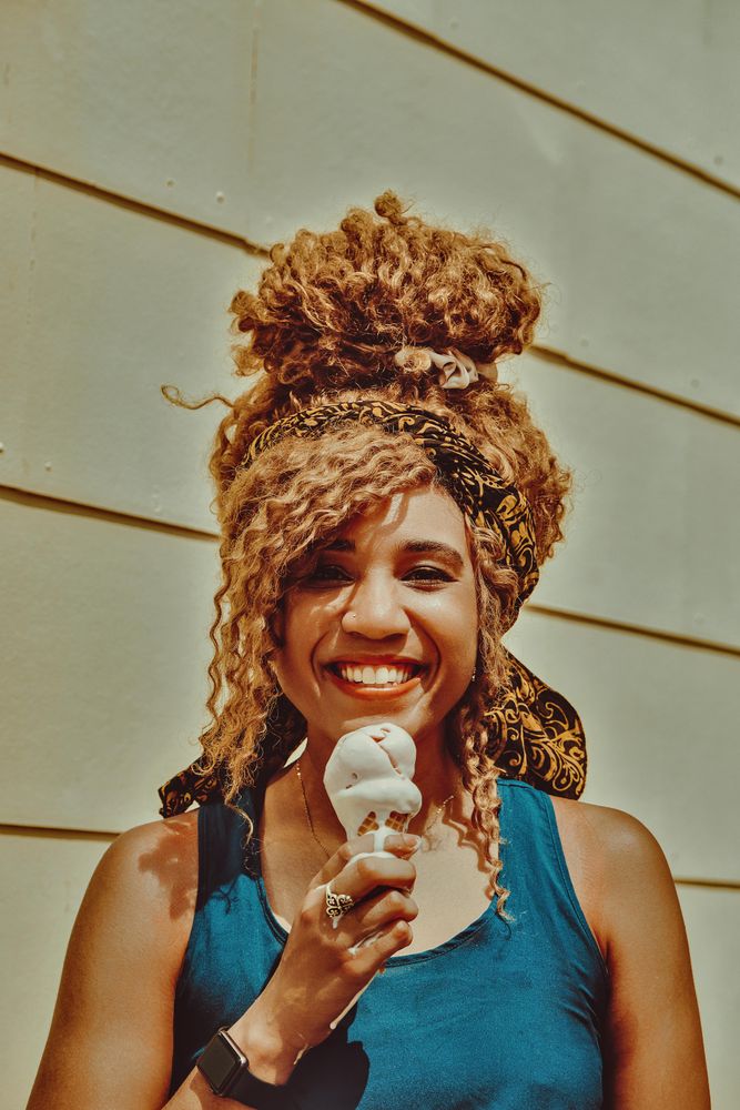 Happy Black female smiling with an ice cream cone in the sun, vertical