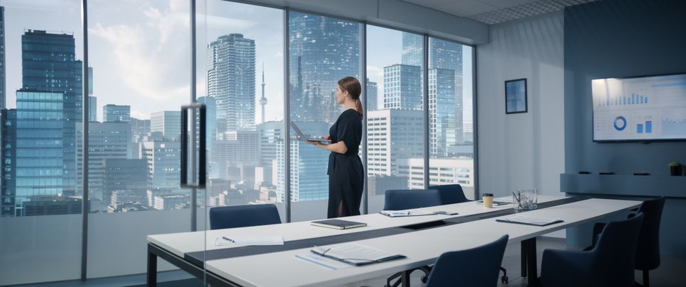 White Businesswoman Standing In Modern Office In Skyscraper With Big City View And Using Laptop Computer.