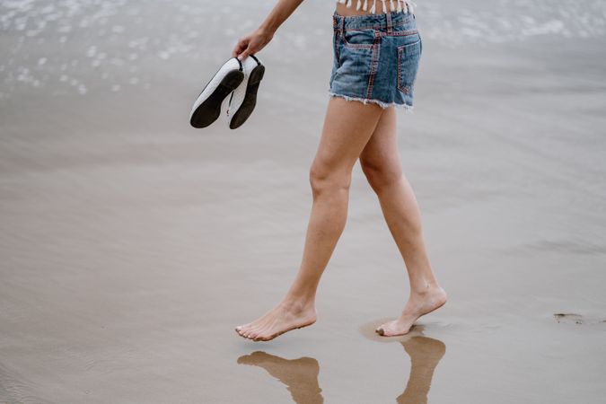 Young female walking barefoot on wet sand