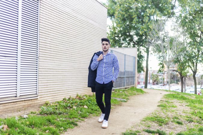 Young man walking next to a building holding a jacket