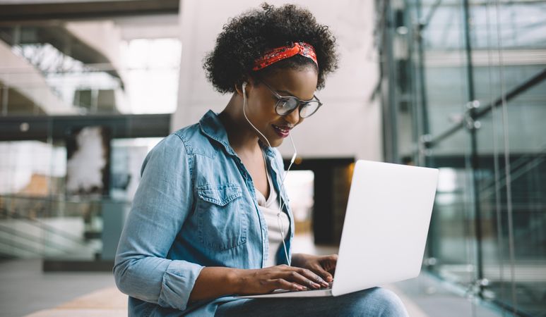 Woman sitting on bench working on laptop wearing earbuds