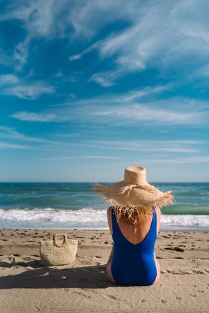 Woman in blue swimsuit and hat on sandy beach