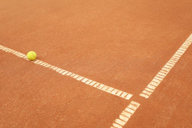Light green tennis ball on clay court, space for text