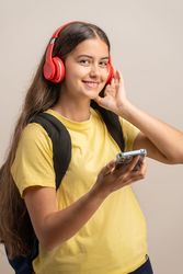 A happy young student listening to music with red headphones and holding a smartphone.