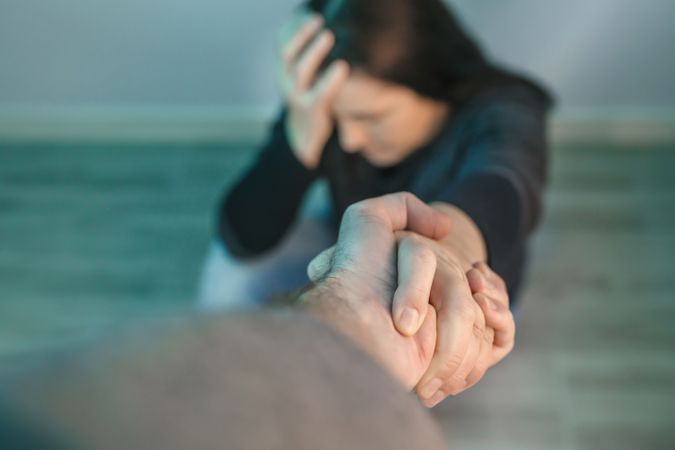 Unrecognizable woman with problems receiving help from man holding her hand