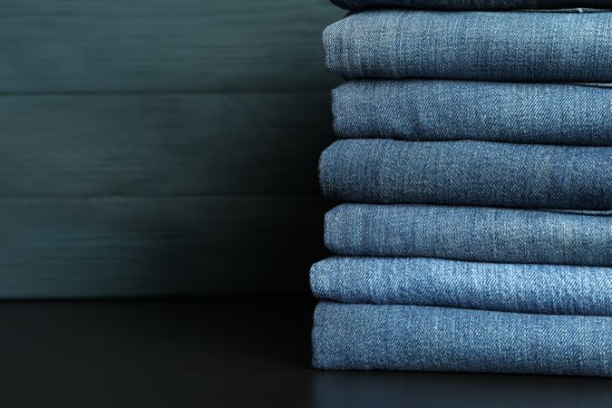Stack of jeans pants on table, space for text