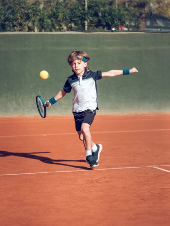 Concentrated child playing tennis on sports court