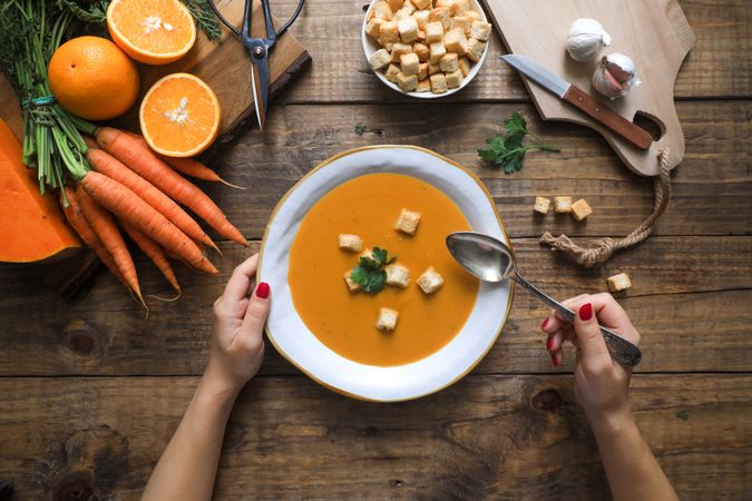 Person hands holding bowl with carrot soup