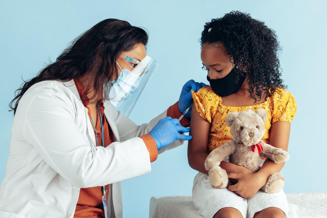 Small girl holding her teddy bear getting covid-19 vaccine from a physician