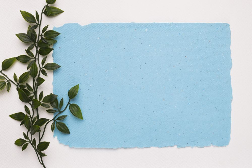 Artificial green twig near blue torn paper light background