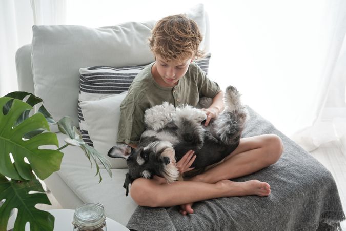 Boy caressing fluffy dog while sitting on sofa