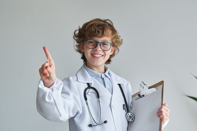 Cheerful boy in medical robe with finger up