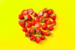 Flat lay composition with strawberries in the shape of heart on color background, space for text