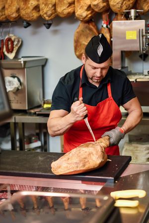 Butcher holding ham and cutting with knife