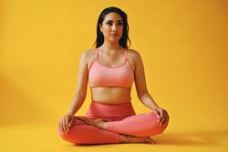 Hispanic female sitting in yoga pose in yellow studio shoot