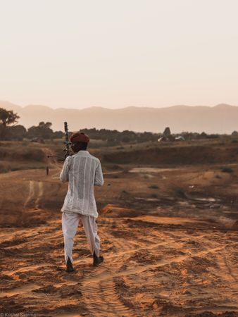 Back view of Indian man wearing turban and kurta standing on dirt land