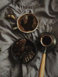 Top view of cup of Turkish coffee surrounded by pine cones on grey bedding