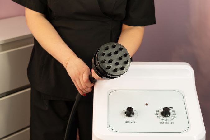 Therapist presenting cavitation handpiece above aesthetic control panel