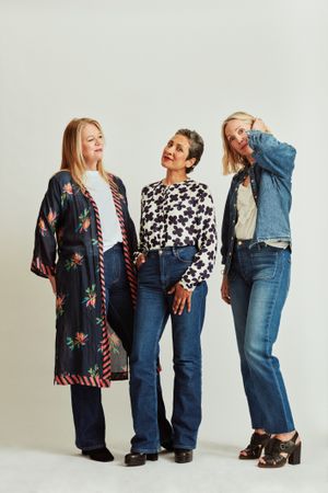 Three happy older women standing together in stylish clothes in studio