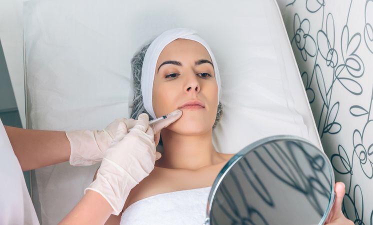 Aesthetician's hand's in latex gloves injecting botox into female's lips in a beauty salon