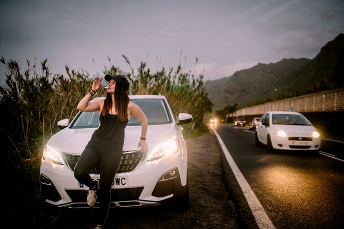 Woman drinking water near car on road at night