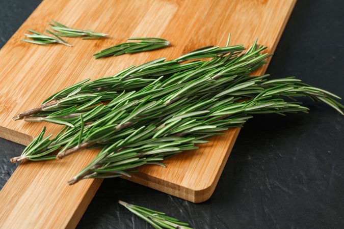 Cutting board with green rosemary on dark background, space for text