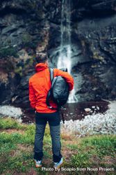 Back view of a man in red jacket with backpack standing facing waterfall 4A9x84