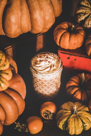 Three frothy drinks with whipped cream topping one table among decorative squashes, top view