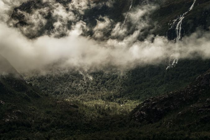 Clouds over green valley between gray mountains
