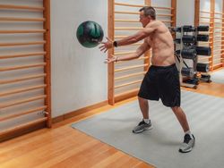 Muscular man throwing ball against wall