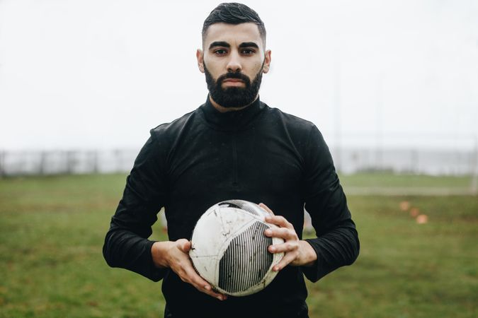 Football player standing on field holding a football in hand
