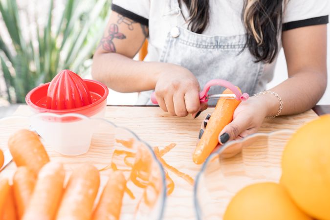 A young Hispanic woman is peeling some carrots to make orange and carrot juice outdoors
