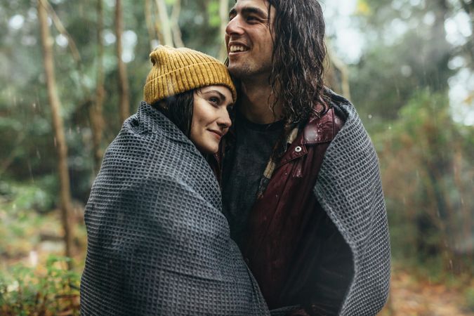 Happy couple hugging under a blanket in the rain