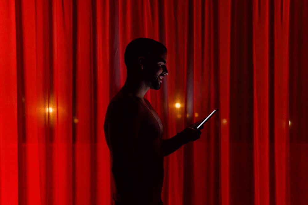 Cheerful man browsing smartphone in darkness