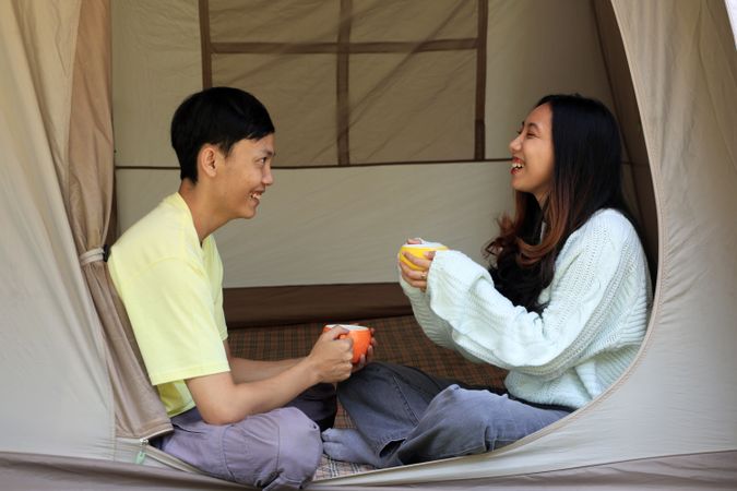 Young Asian Couple Sitting at Tent, Drinking While Chatting.