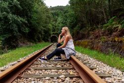 Woman sitting on railway though greenery part of road
