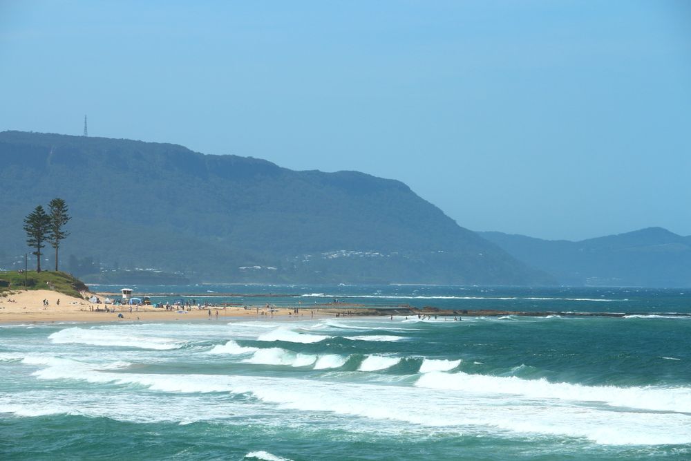 Sandy Beach With Waves Rolling In From The Blue Ocean Under A Clear Blue Sky On A Sunny Day