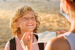 Unrecognizable woman putting mask on cheerful boy