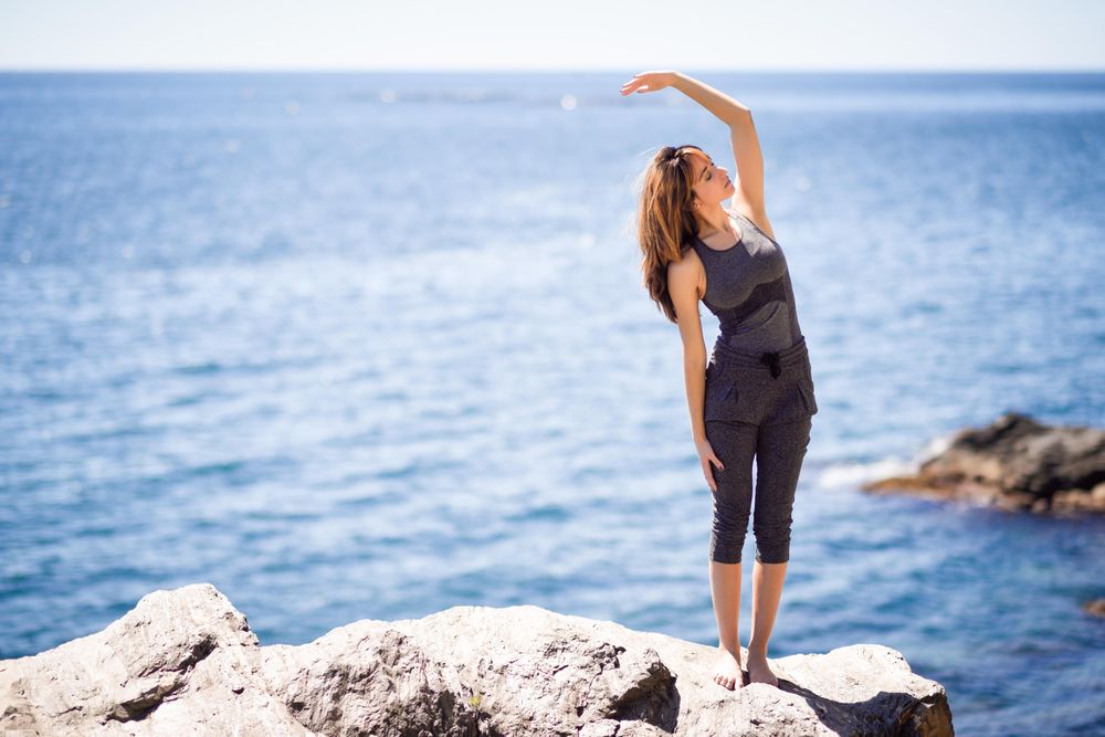 Young woman doing side stretch on the beach, copy space