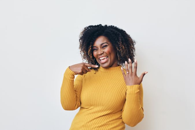 Studio shot of a happy Black woman in yellow shirt showing off her engagement ring