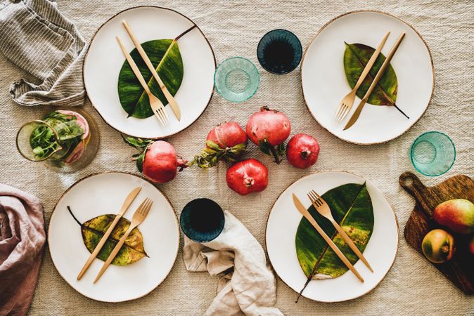 Fresh table setting on brown table cloth, leaves on bright plates, pomegranate, with pitcher