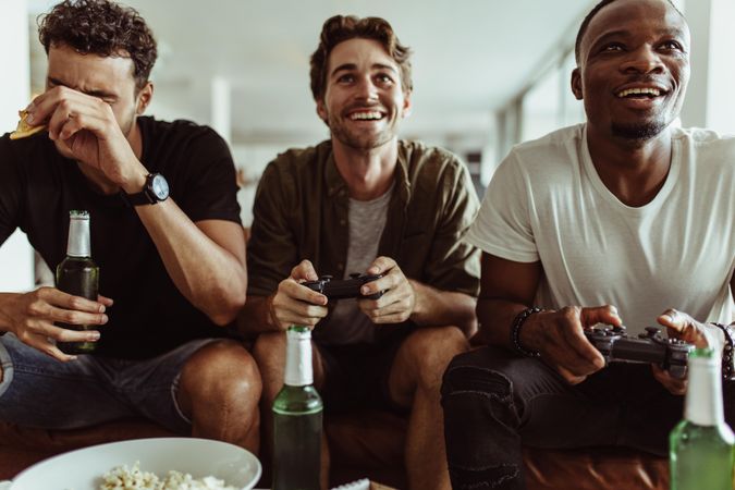 Friends having fun with drinks and snacks while playing video game at home