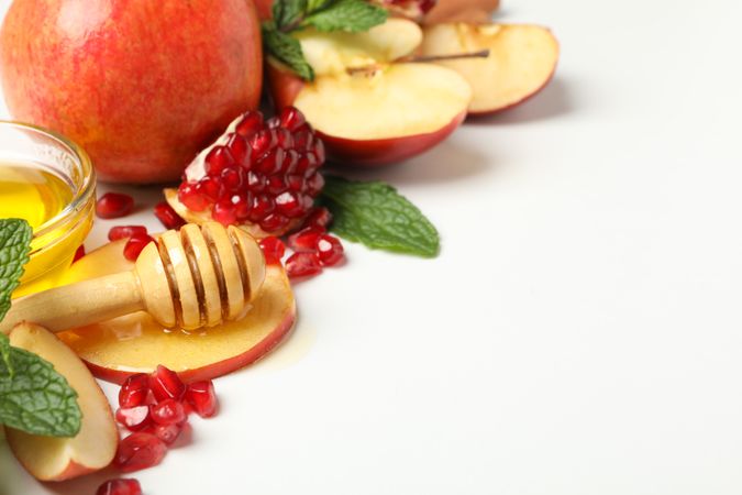 Glass honey pot with dipper, pomegranate, and an apple quarters in corner with copy space