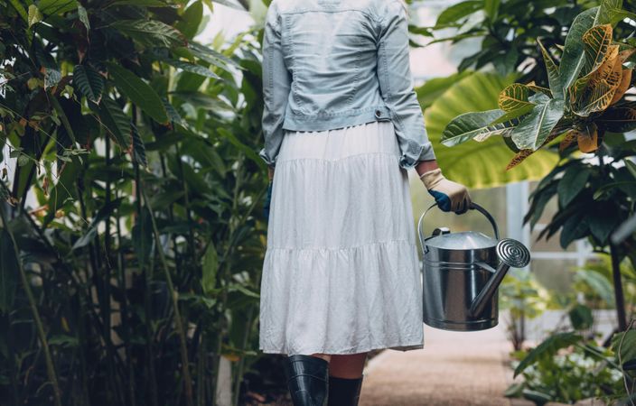Rear view of woman walking with water can in nursery
