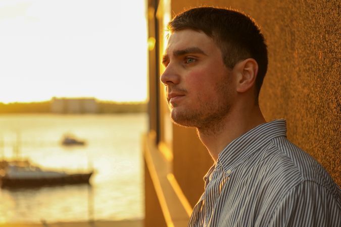 Young man stands leaning against a wall. Amazing sunset