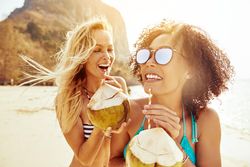 Two women talking and laughing while drinking a tropical cocktail