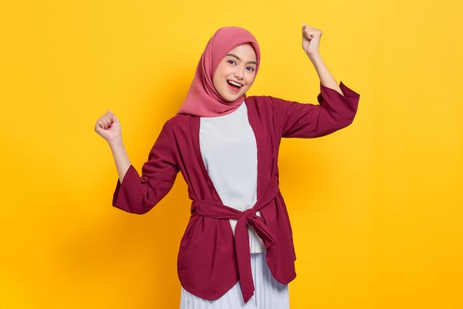 Woman in red headscarf with both arms up in excitement