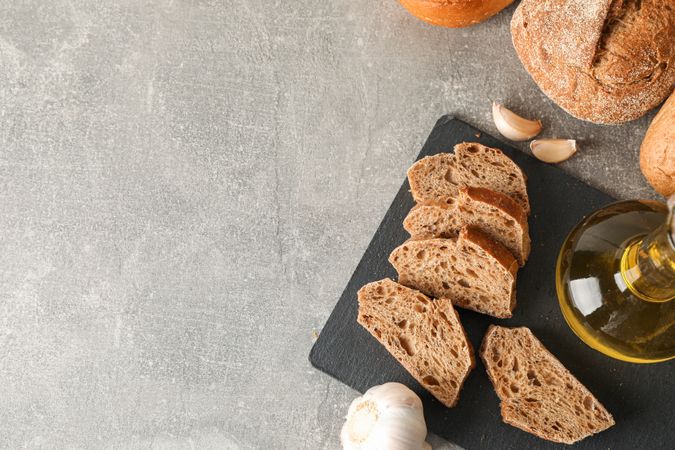 Composition with bakery products, garlic and olive oil on grey background, top view and space for text