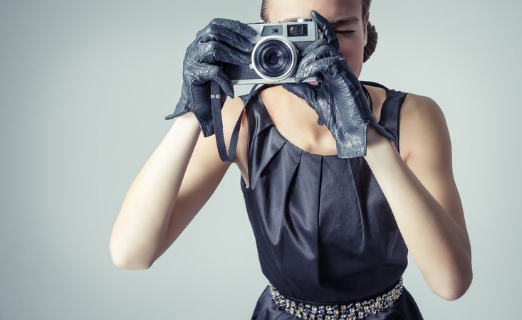 Model in vintage clothing and gloves taking picture with camera